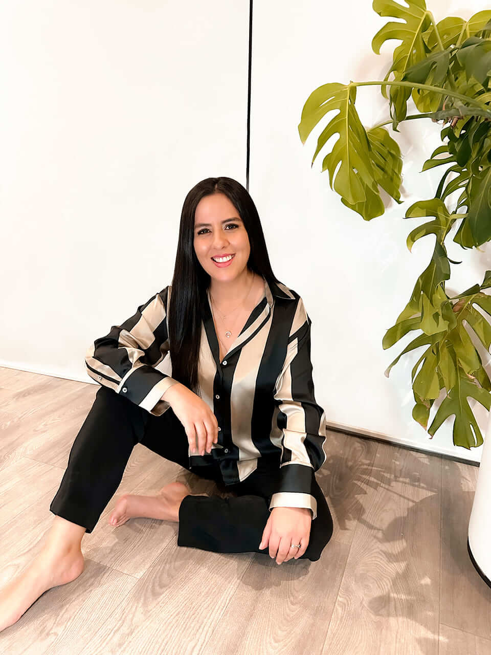 Naty descalza sentada en el piso junto a una planta